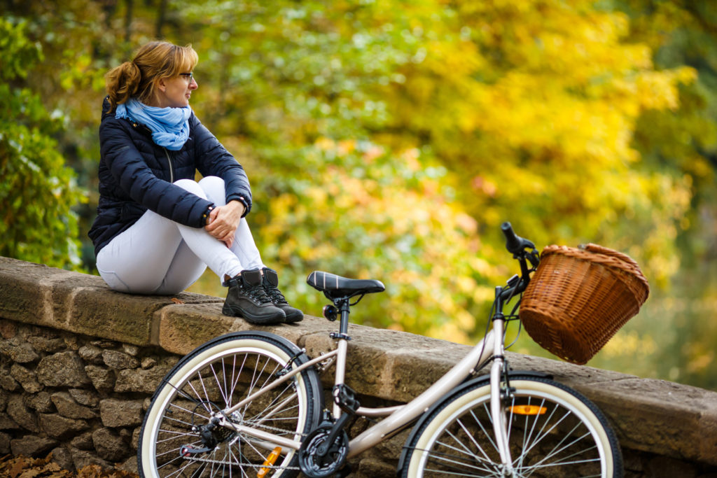 Women sitting on a bridge in the fall next to her bike