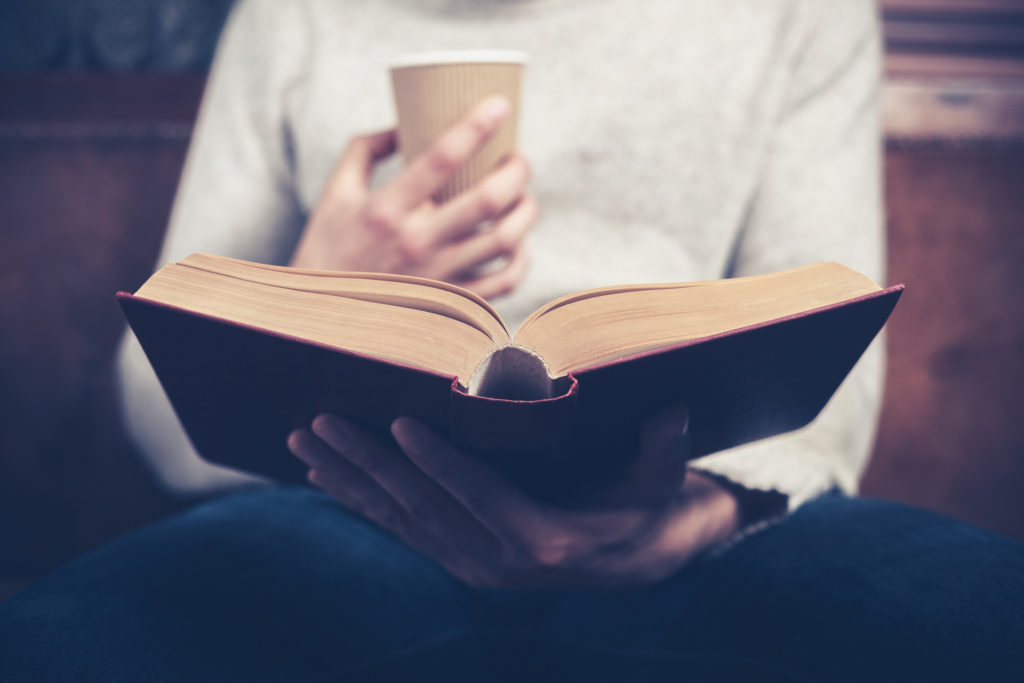 Person drinking coffee while reading a book